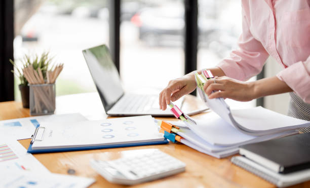 Hands organizing paperwork with colorful tabs at a sunlit desk