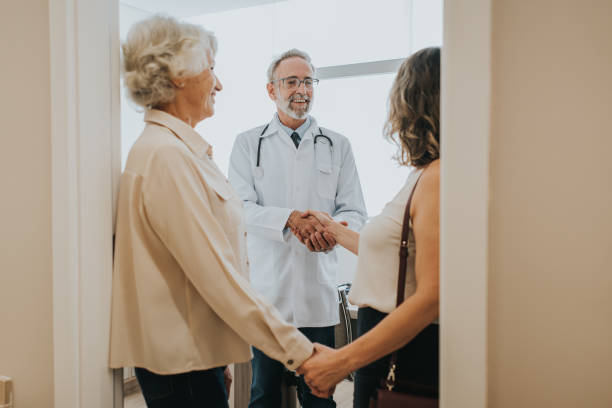 A smiling doctor greeting a senior woman and her adult daughter at the office doorway